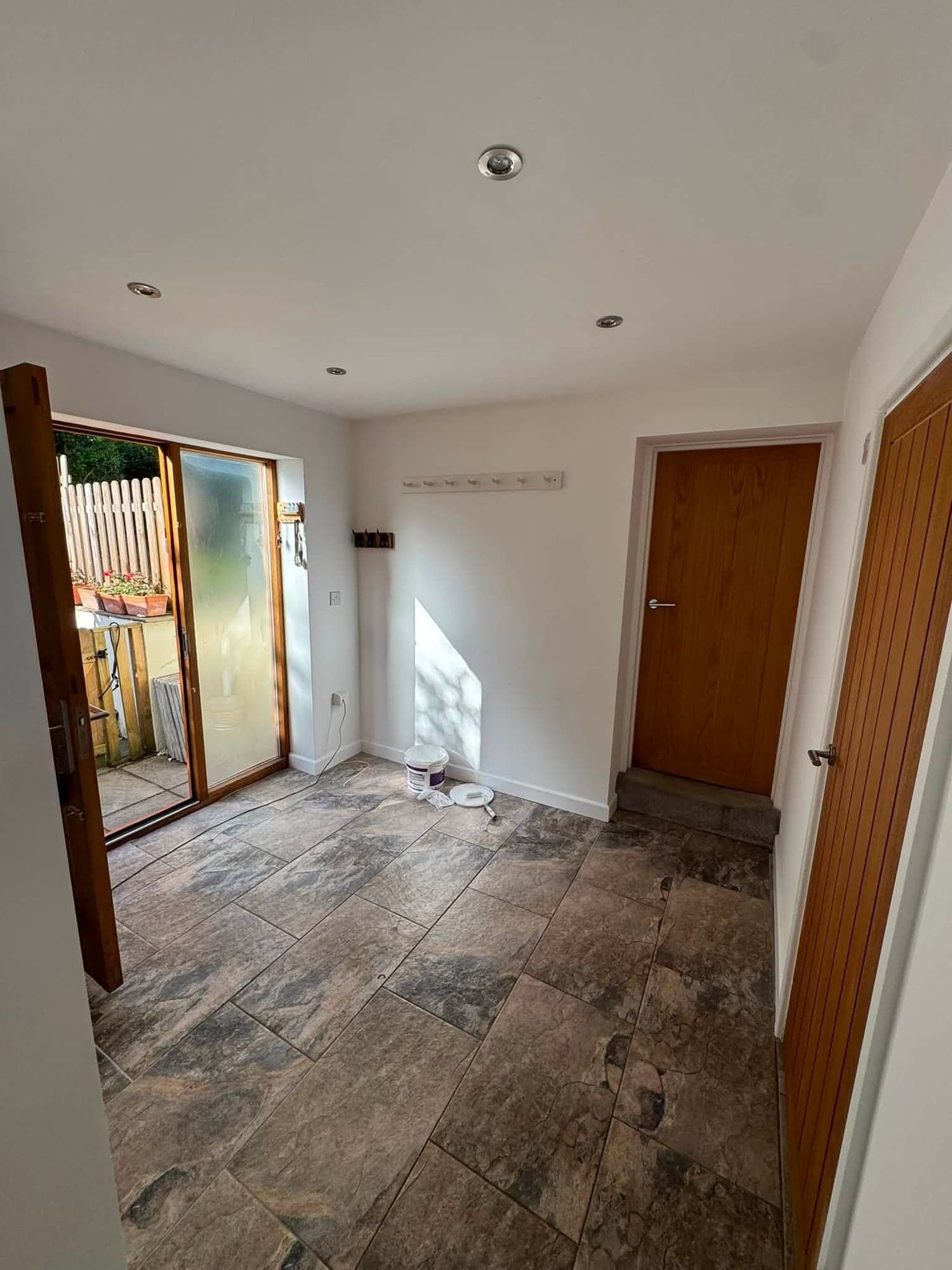 Boot room with white painted walls and ceiling, oak internal doors, glazed garden doors and a slate floor