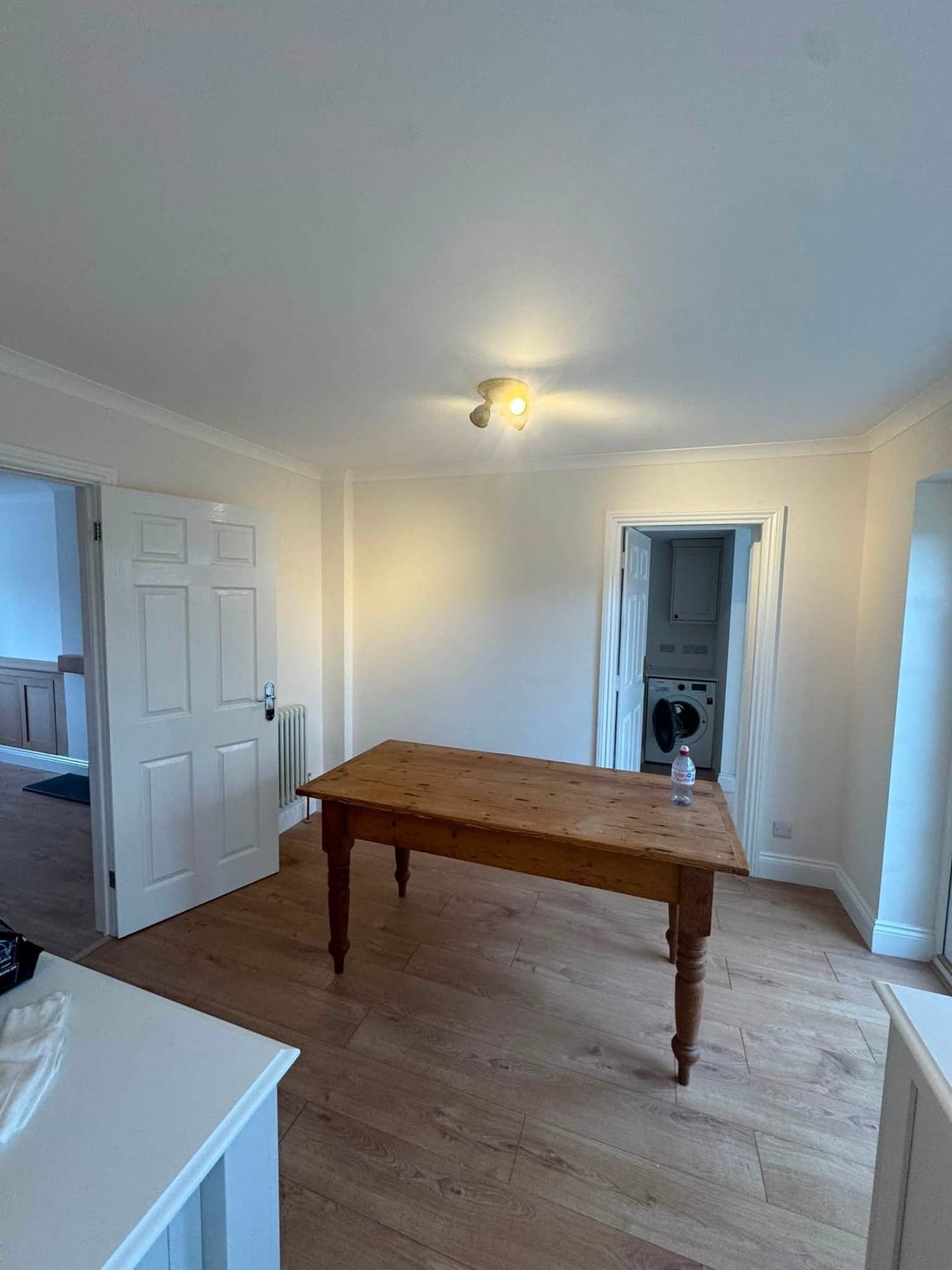 Dining room with freshly painted white walls and woodwork, a white panelled door, a pine table and an oak floor