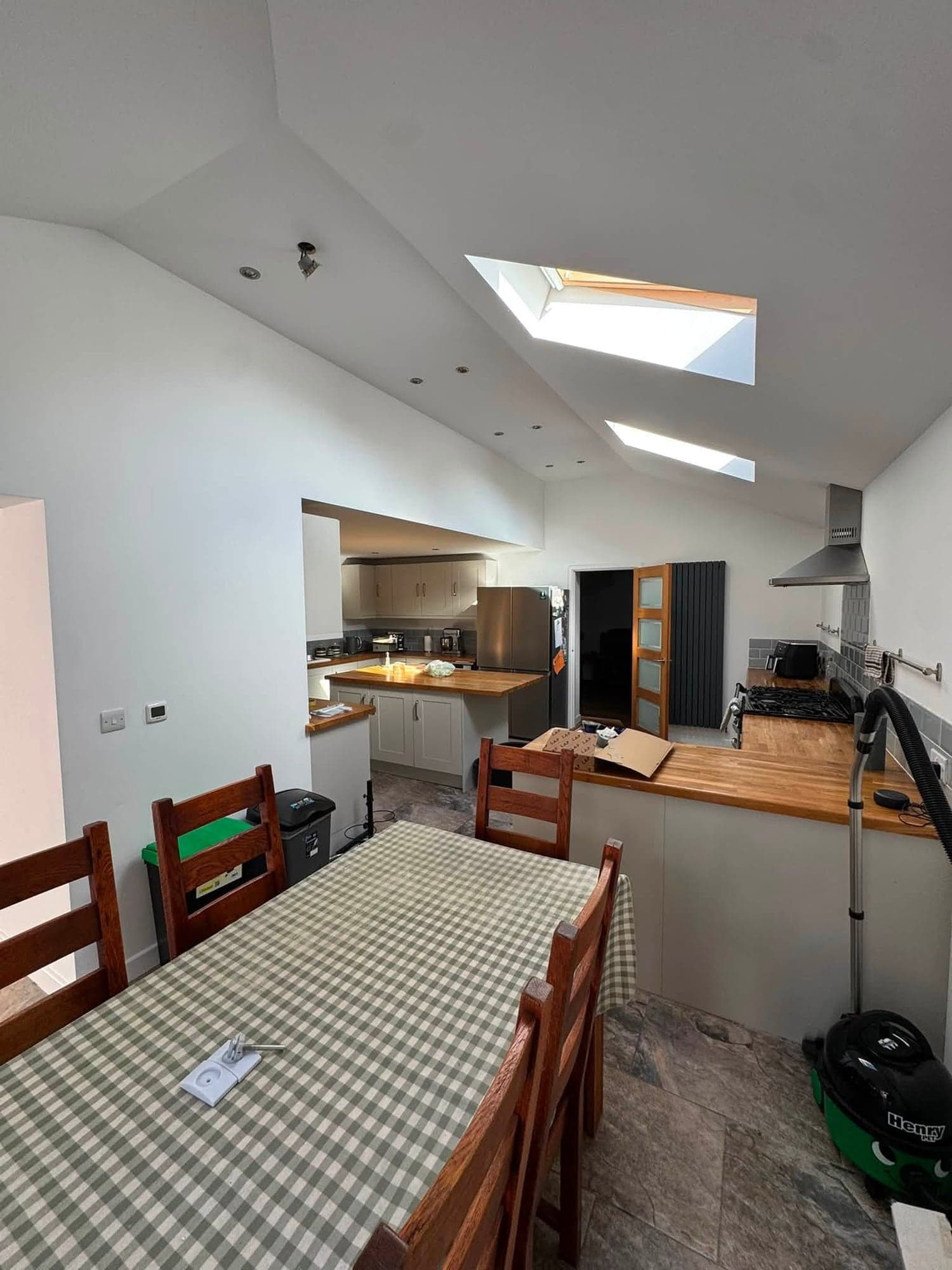 Dining end of a kitchen extension with a gingham-covered table, white sloping ceiling with two rooflights and the kitchen beyond