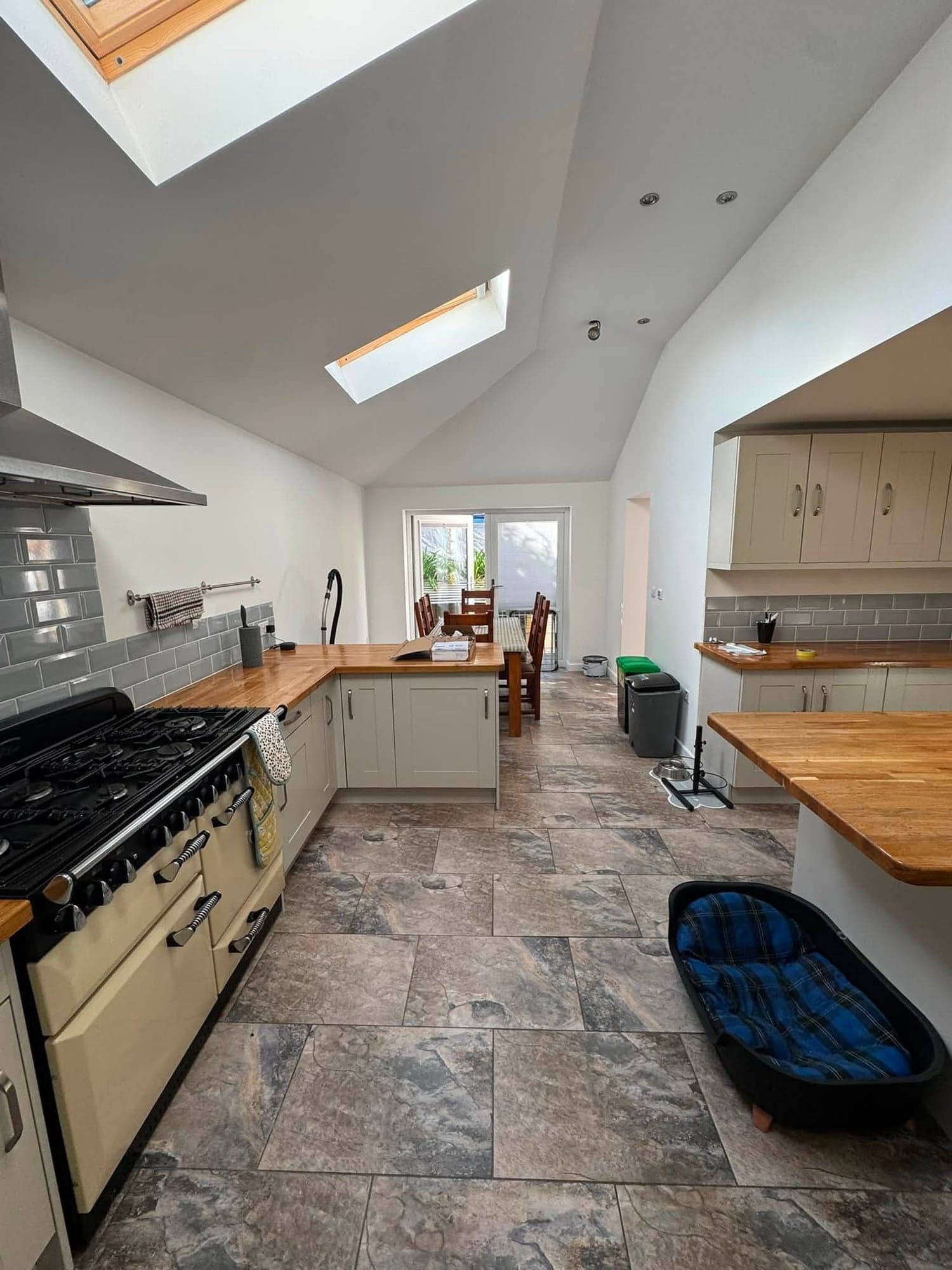 Kitchen with a cream range cooker, grey metro tiles and painted units under a white vaulted ceiling with rooflights, looking through to the dining area