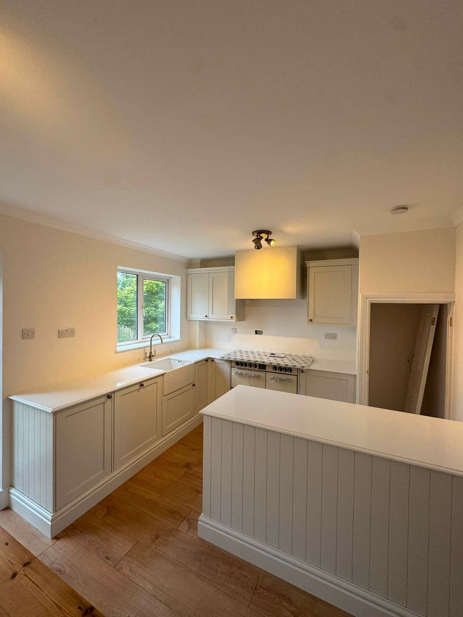 Kitchen with hand-painted pale cream shaker cabinets, white walls and ceiling, a white worktop and an oak floor