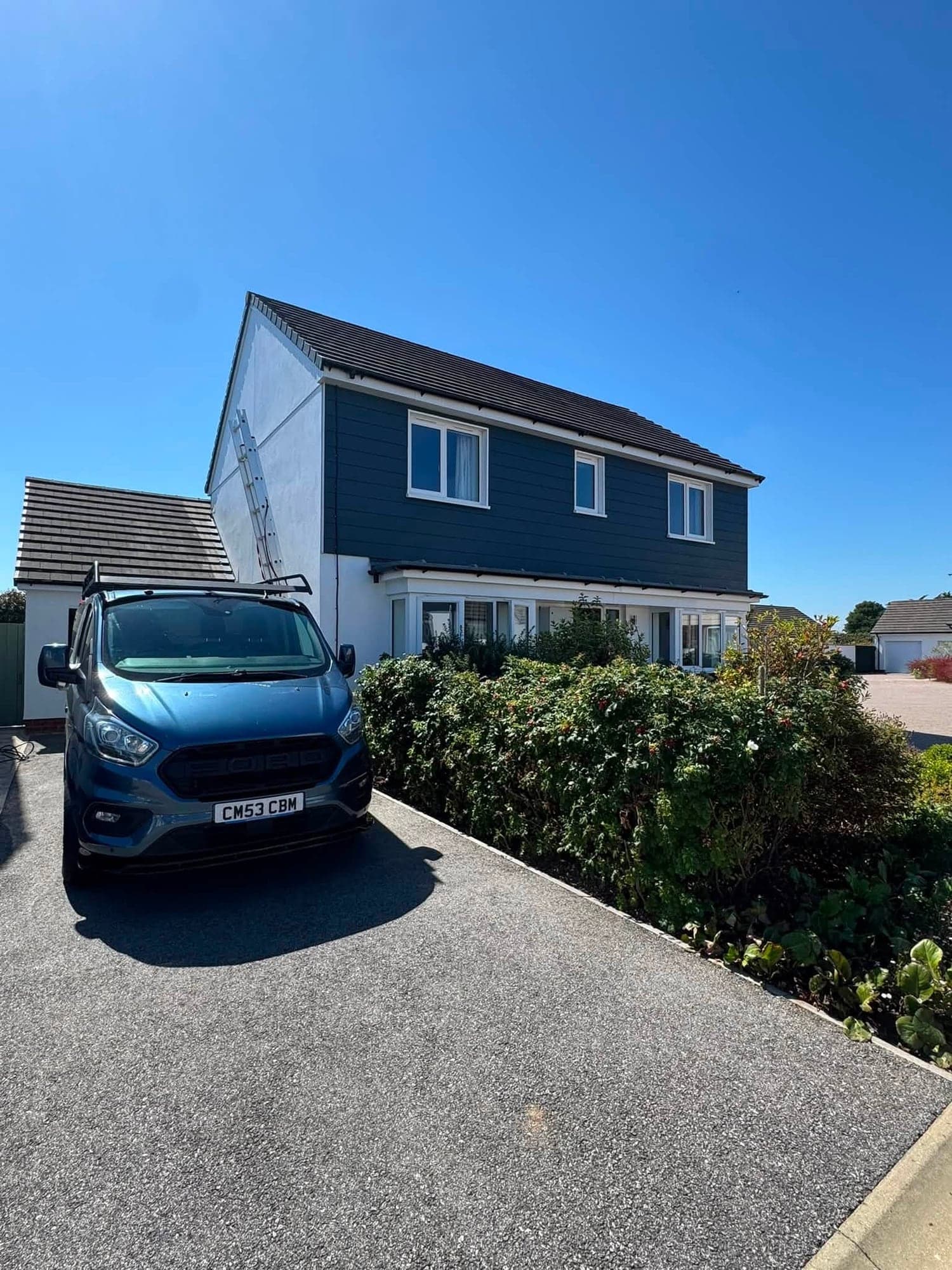 Front of a white rendered house with navy cladding on the upper floor and a bay window, a decorator's van on the drive