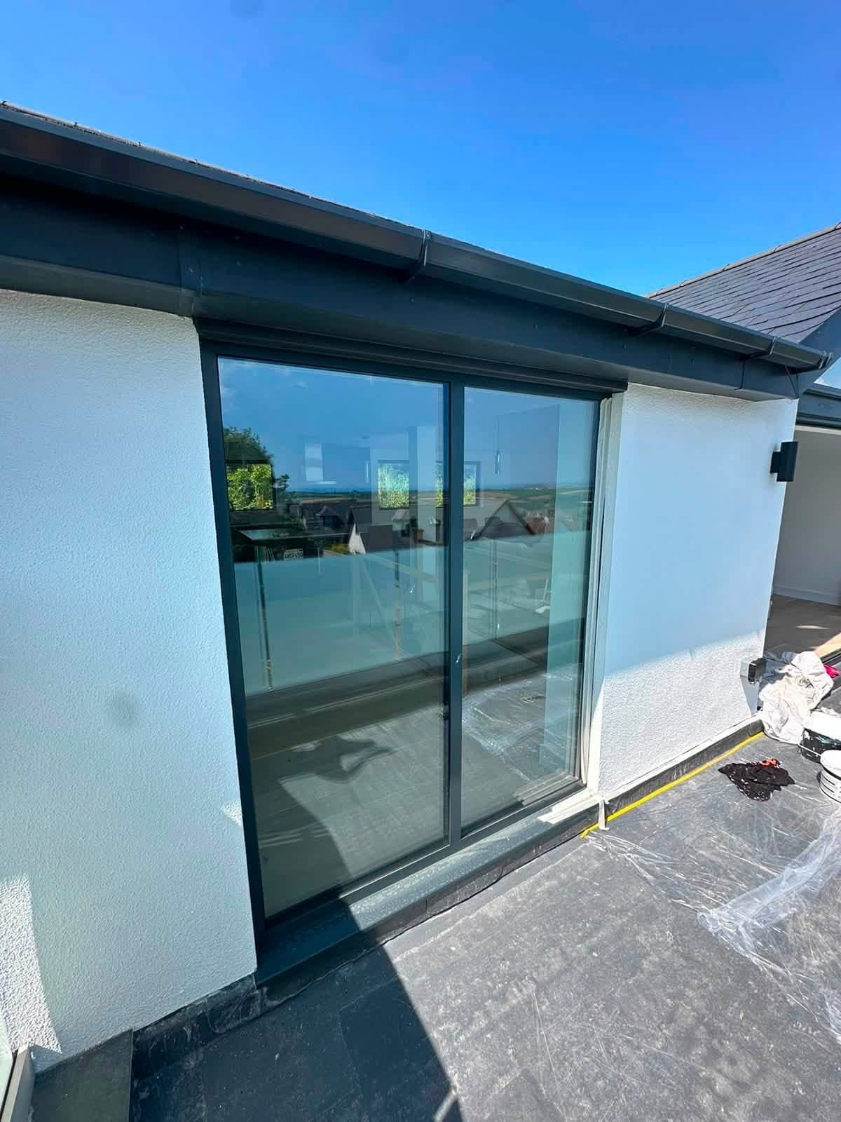 Freshly painted white render around dark grey aluminium sliding doors on a first-floor balcony, with dark fascia above